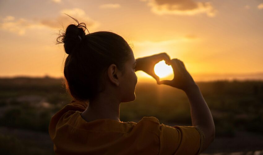 A silhouette of a young woman forming a heart shape at sunset in Kelâat M'Gouna, Morocco.